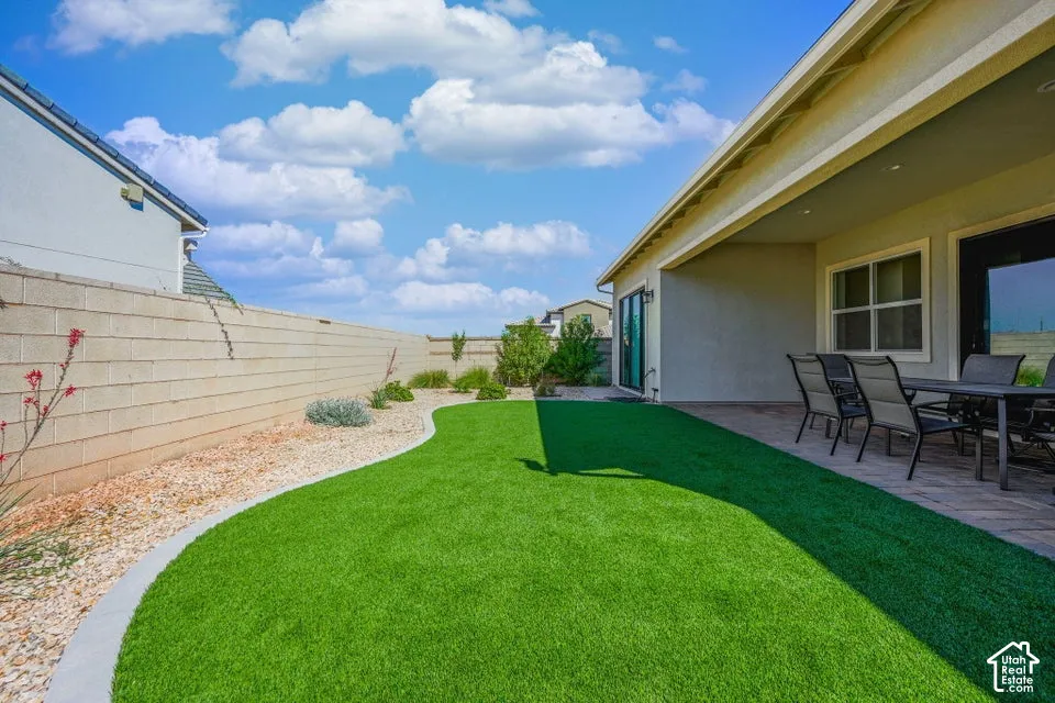 Expansive artificial turf lawn with a paved patio area, covered outdoor living space, and a block privacy wall