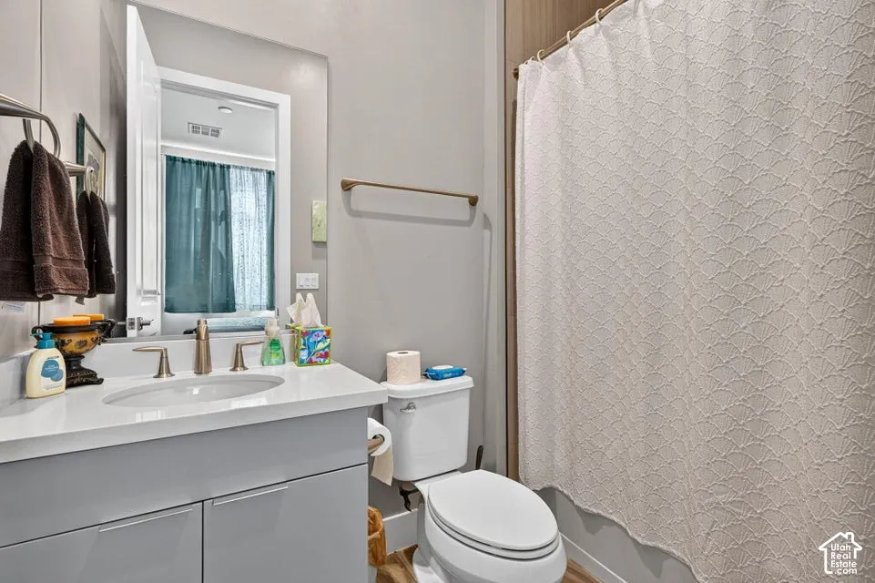 Vanity with undermount sink and brushed nickel faucet, large mirror, and toilet with wood-finish flooring