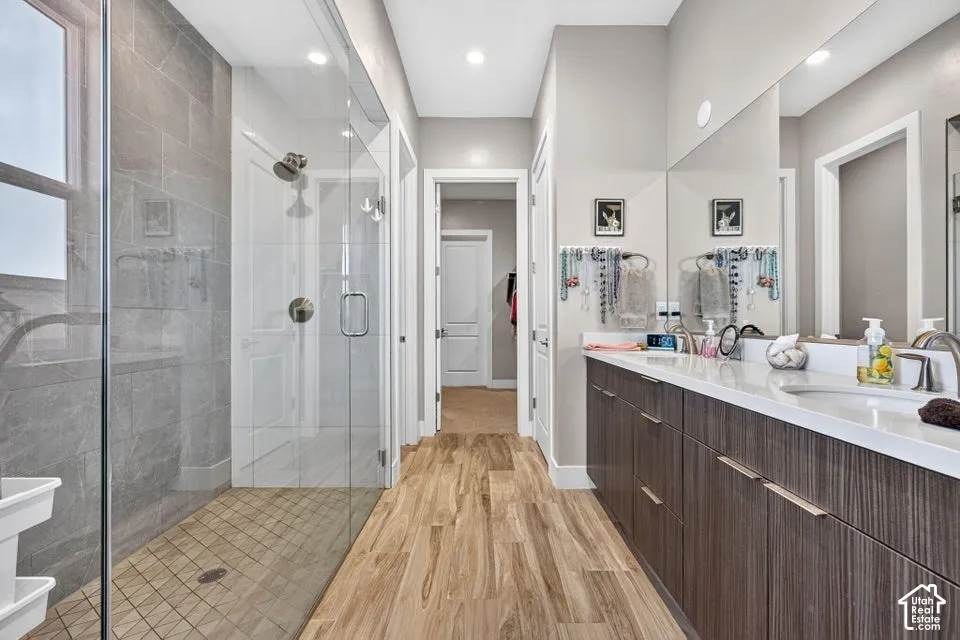 Full-height mirrors, an extended dual vanity, wood-finish flooring, a glass-enclosed shower, and a tiled shower surround