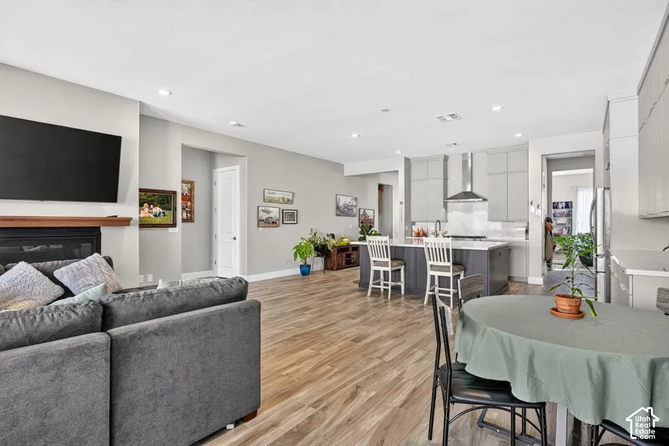 Recessed lighting, wood-finish flooring, fireplace with wood mantel, kitchen island with seating, and stainless steel range hood