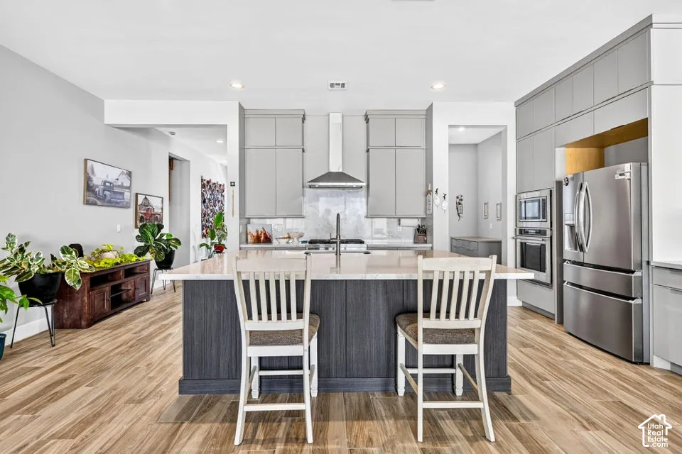 Spacious kitchen featuring an island with a light-toned countertop, wood-finish flooring, light grey cabinetry, stainless steel appliances, and recessed lighting
