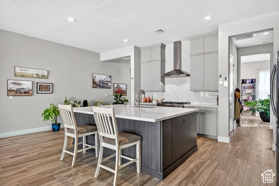 Kitchen featuring wood-finish flooring, a central island with white countertop, light gray cabinetry, and stainless steel range hood