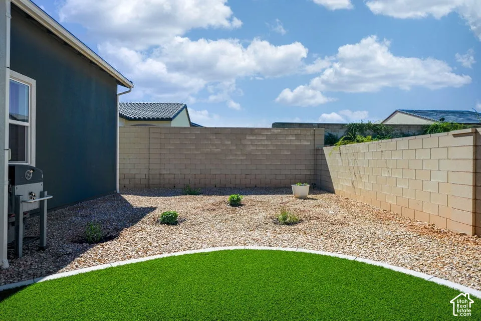 Backyard featuring artificial turf, gravel landscaping, a window, and a block wall