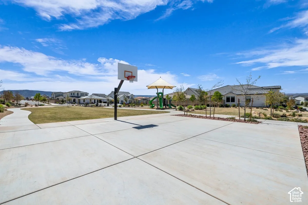 Concrete basketball half-court, adjacent green space, paved walking path, and a covered playground structure