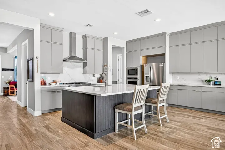 Gray cabinetry with crown molding, stainless steel appliances, a center island with a white countertop, wood-finish flooring, and a white backsplash