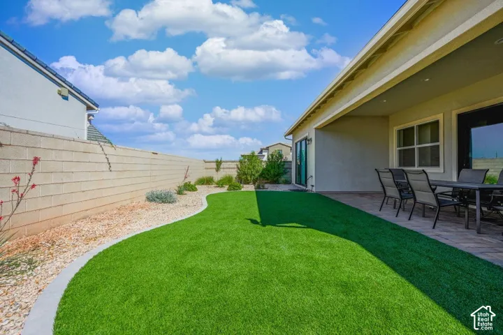 Expansive artificial turf lawn with a paved patio area, covered outdoor living space, and a block privacy wall