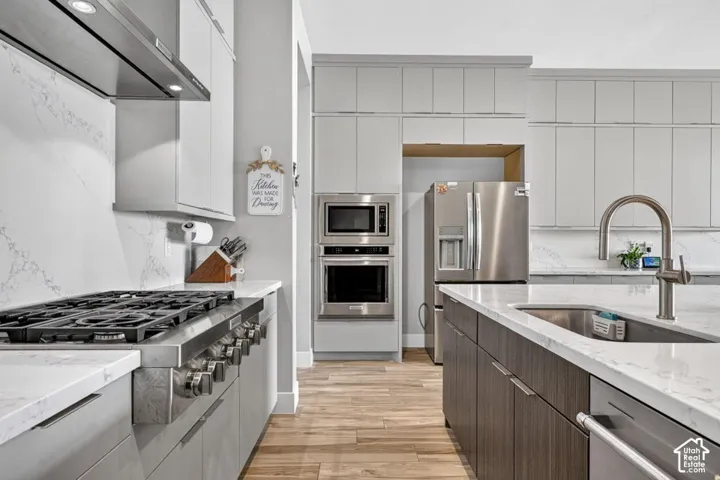 Contemporary kitchen with light gray cabinetry, stainless steel appliances, a gas range with a matching range hood, and light-toned countertops