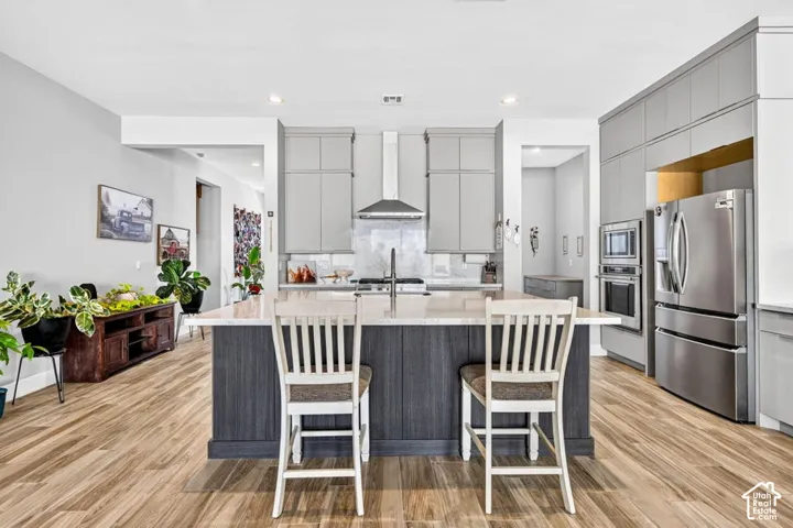 Spacious kitchen featuring an island with a light-toned countertop, wood-finish flooring, light grey cabinetry, stainless steel appliances, and recessed lighting