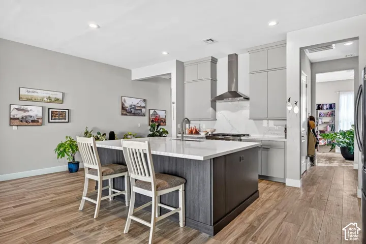 Kitchen featuring wood-finish flooring, a central island with white countertop, light gray cabinetry, and stainless steel range hood