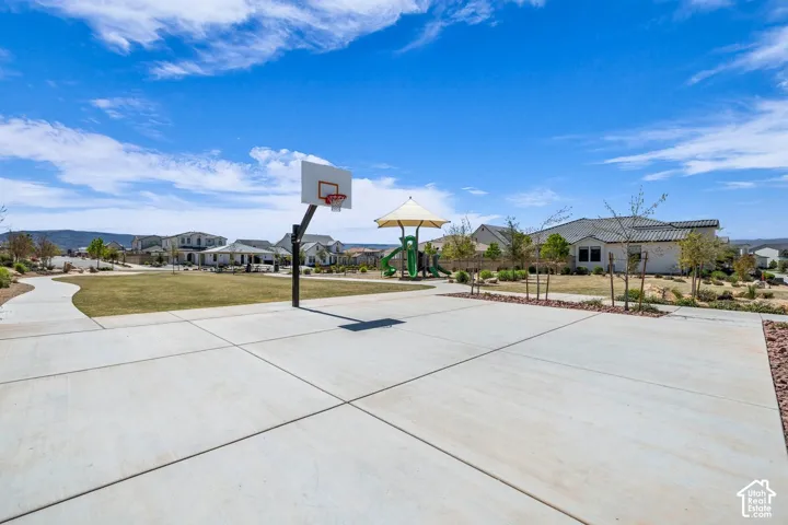 Concrete basketball half-court, adjacent green space, paved walking path, and a covered playground structure