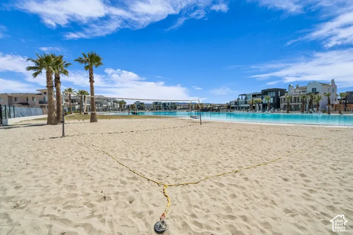 Expansive sandy area featuring a beach volleyball court with a net, bordered by palm trees