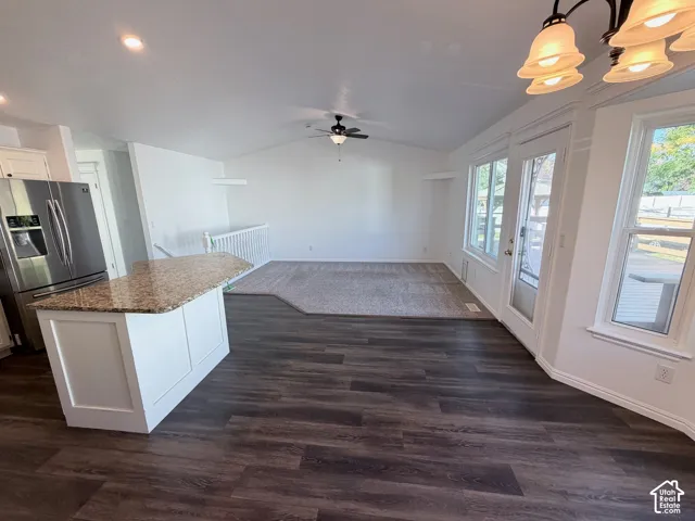 Open-concept living space featuring LVP flooring, a kitchen island with stone-look countertop, stainless steel refrigerator, and vaulted ceilings with a ceiling fan
