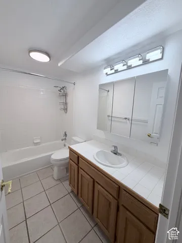 Ceramic tile flooring, white subway tile shower surround, wood-finish vanity with tiled countertop, recessed medicine cabinet, and contemporary vanity lighting