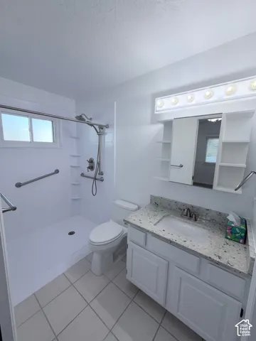 Walk-in shower with grab bars, single-handle shower fixture, white vanity with stone-finish countertop, single basin sink, and tile flooring