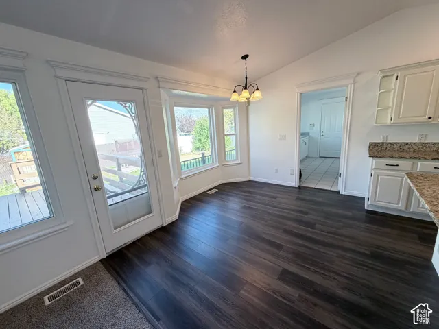 Dark LVP flooring, vaulted ceiling, bay window, glass-panel door, and white cabinetry with granite countertops