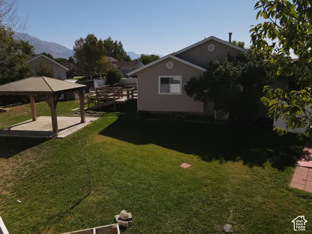 Expansive green space featuring a built-in wooden gazebo with a concrete pad, a multi-level wooden deck, and mature trees