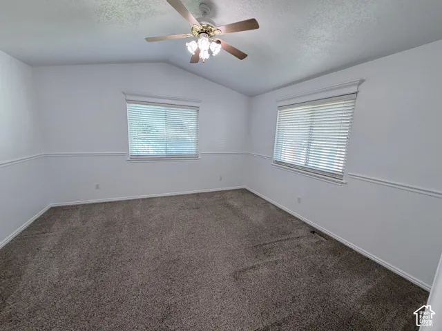 Vaulted ceiling, two windows with blinds, ceiling fan with light fixture, chair rail molding, and carpeted flooring
