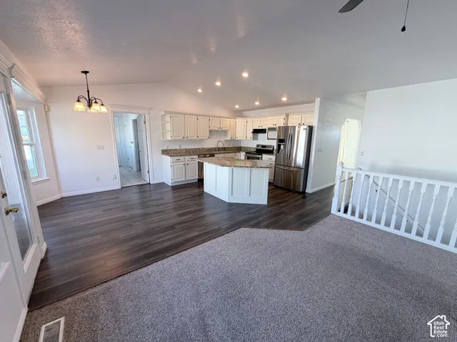 Vaulted ceilings with recessed lighting, LVP flooring, white cabinetry, integrated stainless steel appliances, and a kitchen island with stone countertops