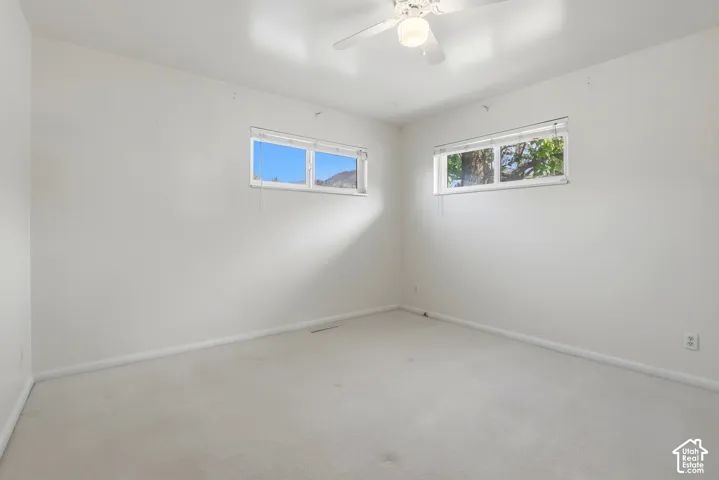 Wall-to-wall carpeting, white walls, two horizontal windows, and a ceiling fan with integrated lighting