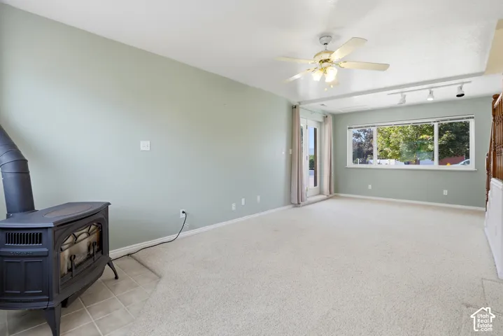 Expansive room with neutral carpeting, a black cast iron stove on tiled flooring, and a ceiling fan