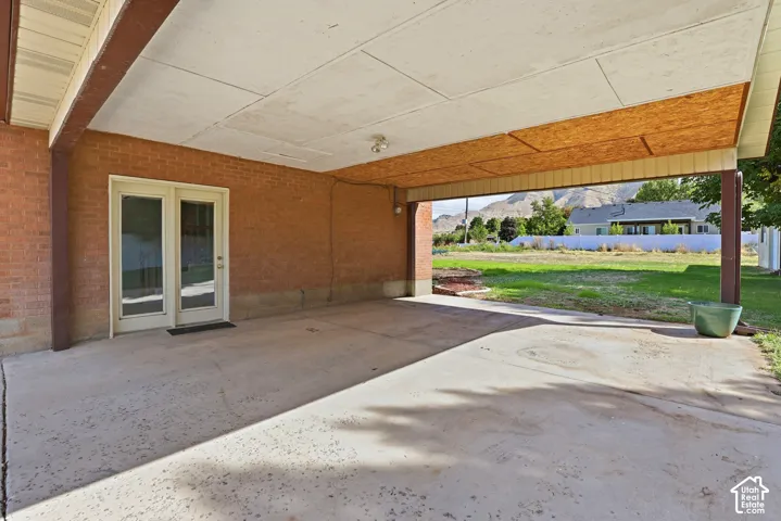Covered patio area with concrete surfacing, brick exterior wall, and double glass-panel doors