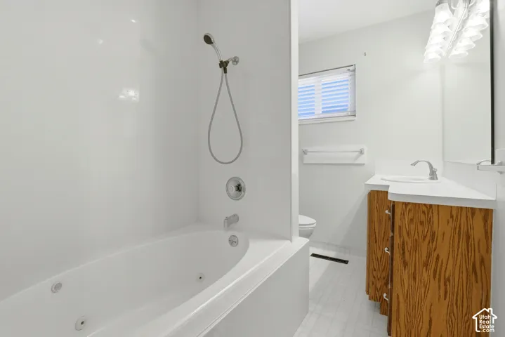 Jetted bathtub with an integrated shower, wood-finish vanity with countertop sink, and overhead vanity lighting