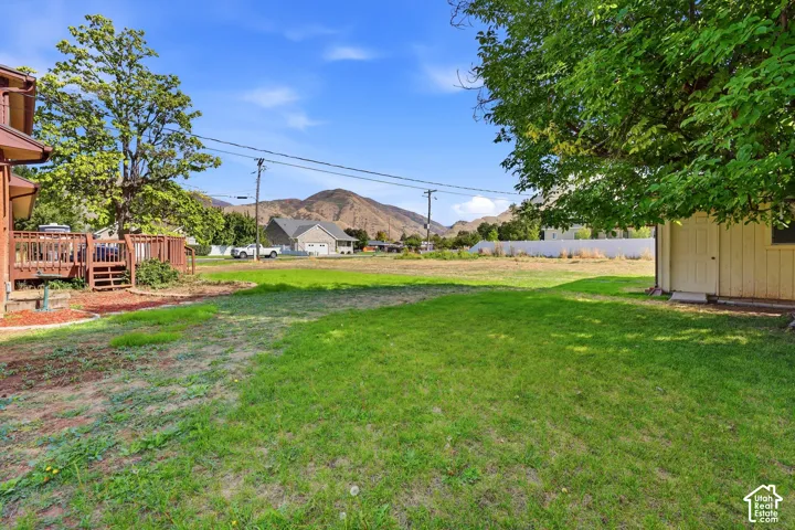 Expansive green lawn with a wood-finished shed, a multi-level wood-finished deck, and a mountainous backdrop