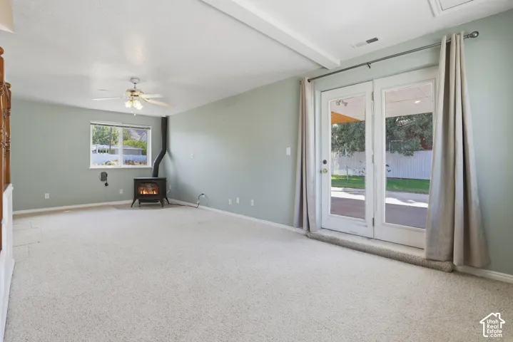 Wood-burning stove, ceiling fan, carpet flooring, window with exterior exposure, and double French doors to the exterior