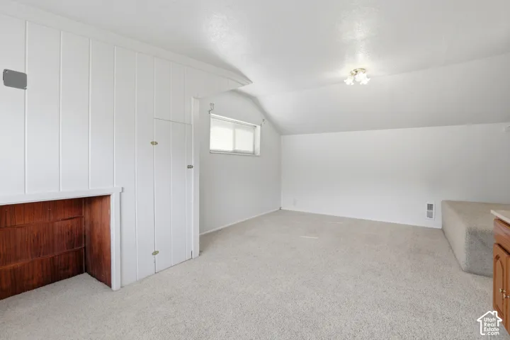 Sloped ceilings with a flush mount light fixture, carpeting, wood-paneled walls, and built-in cabinetry
