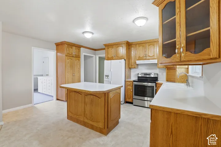 Kitchen featuring wood cabinetry, a center island with white countertops, stainless steel range, and a white refrigerator