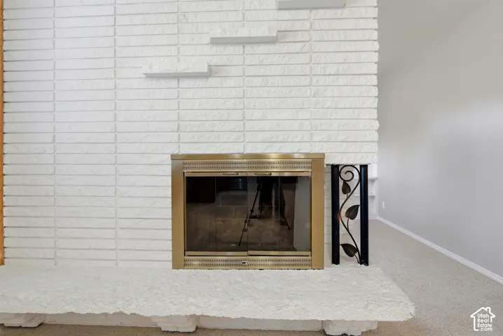 White brick fireplace featuring a brass surround, decorative metalwork, and a textured hearth