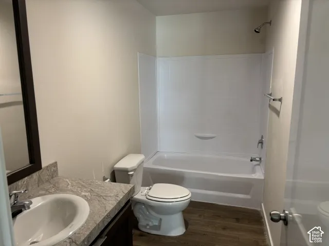Bathroom featuring a shower/tub combination, single vanity with a mounted sink, dark wood-finish cabinetry, and wood-finish flooring
