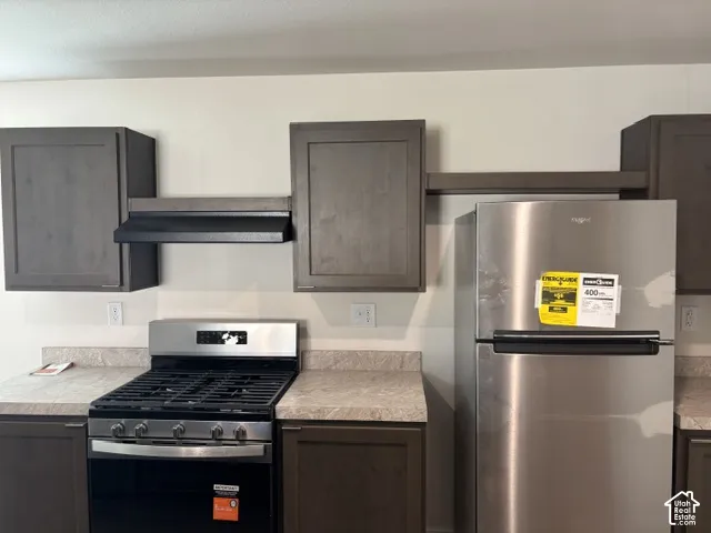 Stainless steel gas range, stainless steel refrigerator, dark wood-finish cabinetry, and light-toned countertops