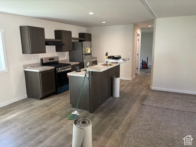 Open-concept kitchen featuring dark wood-finish cabinetry, light-toned countertops, a stainless steel refrigerator, and a kitchen island with seating