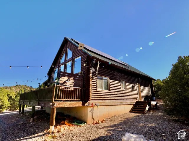 Log cabin exterior with an elevated wood deck, A-frame window design, and a solar panel array on the roof