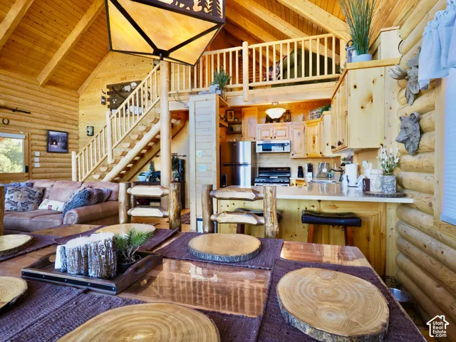 Open-concept living space with vaulted wood-plank ceilings, a log staircase, and a wood-finish kitchen featuring a breakfast bar