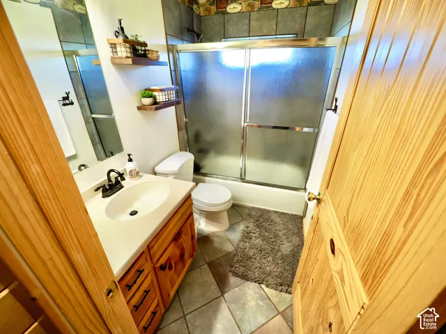 Wood-paneled door, vanity with integrated sink, tiled flooring, tiled shower surround, and sliding glass shower door