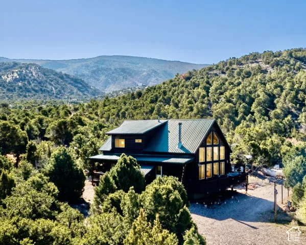 Mountain cabin featuring a dark-toned exterior, a green metal roof, a wrap-around porch, and a prominent A-frame window design