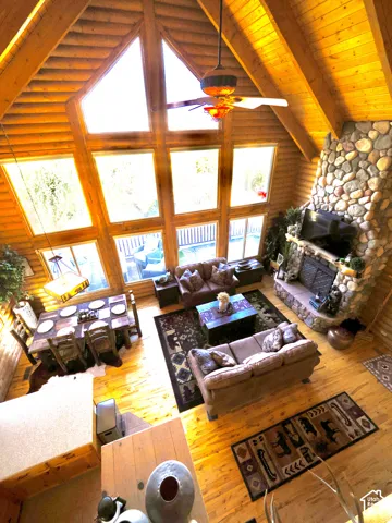 Vaulted wood-paneled ceilings, a floor-to-ceiling stone fireplace, large picture windows, wood-finish flooring, and a ceiling fan with light fixture