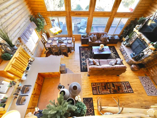 Vaulted ceiling with exposed wood beams, expansive floor-to-ceiling windows, wood-finish flooring, stone fireplace, and built-in kitchen cabinetry