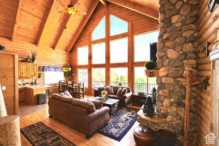 Vaulted ceilings with exposed wood beams, floor-to-ceiling windows, natural wood-finish walls, a prominent stone fireplace, and wood-finish flooring throughout