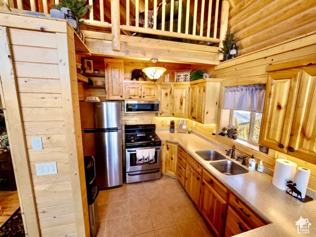 Kitchen featuring wood cabinetry, stainless steel appliances, a double basin sink, and tile flooring