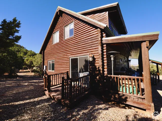 Log cabin exterior with prominent log siding, multiple windows, a covered porch, and a raised wooden deck