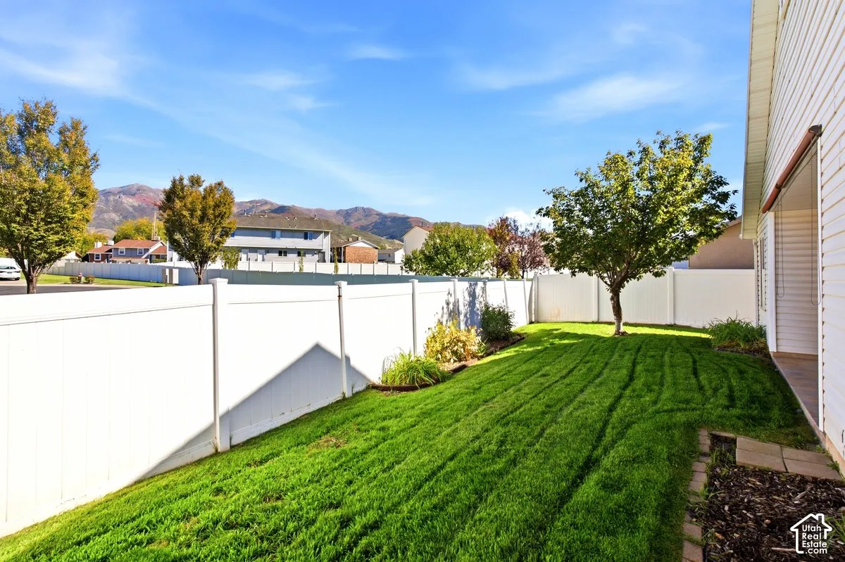 Expansive backyard featuring a manicured lawn, white privacy fencing, and mature trees