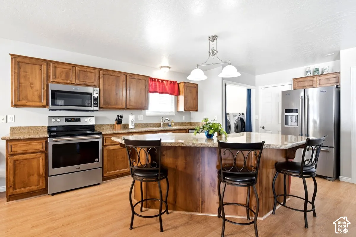Kitchen featuring wood-finish cabinetry, stainless steel appliances, granite-style countertops, wood-finish flooring, and a kitchen island with seating
