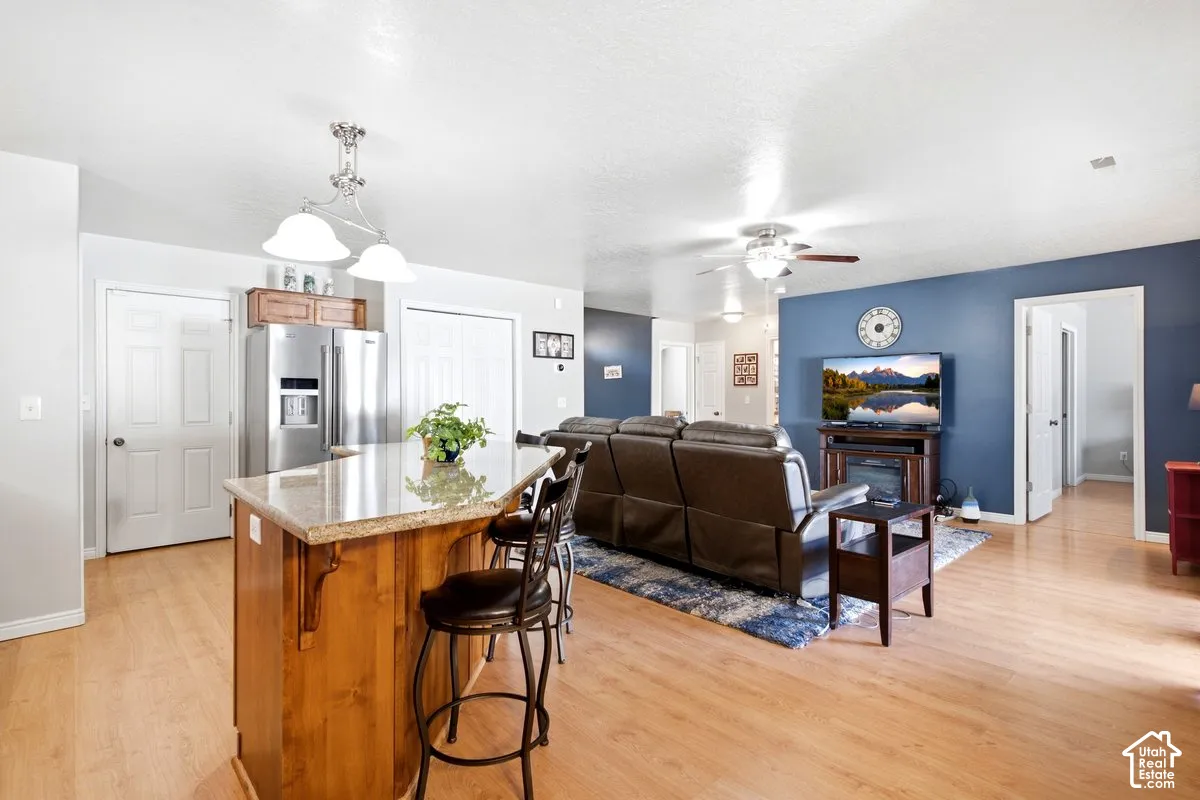 Kitchen island with granite-style countertop, wood-finish flooring throughout, stainless steel refrigerator, white doors, and ceiling fan