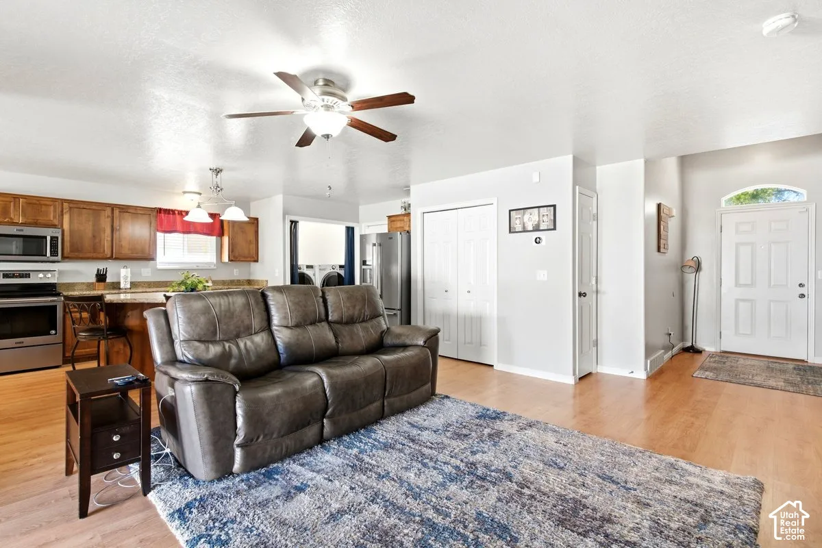 Open-concept living area featuring wood-finish flooring, a ceiling fan with integrated lighting, and a kitchen with stainless steel appliances