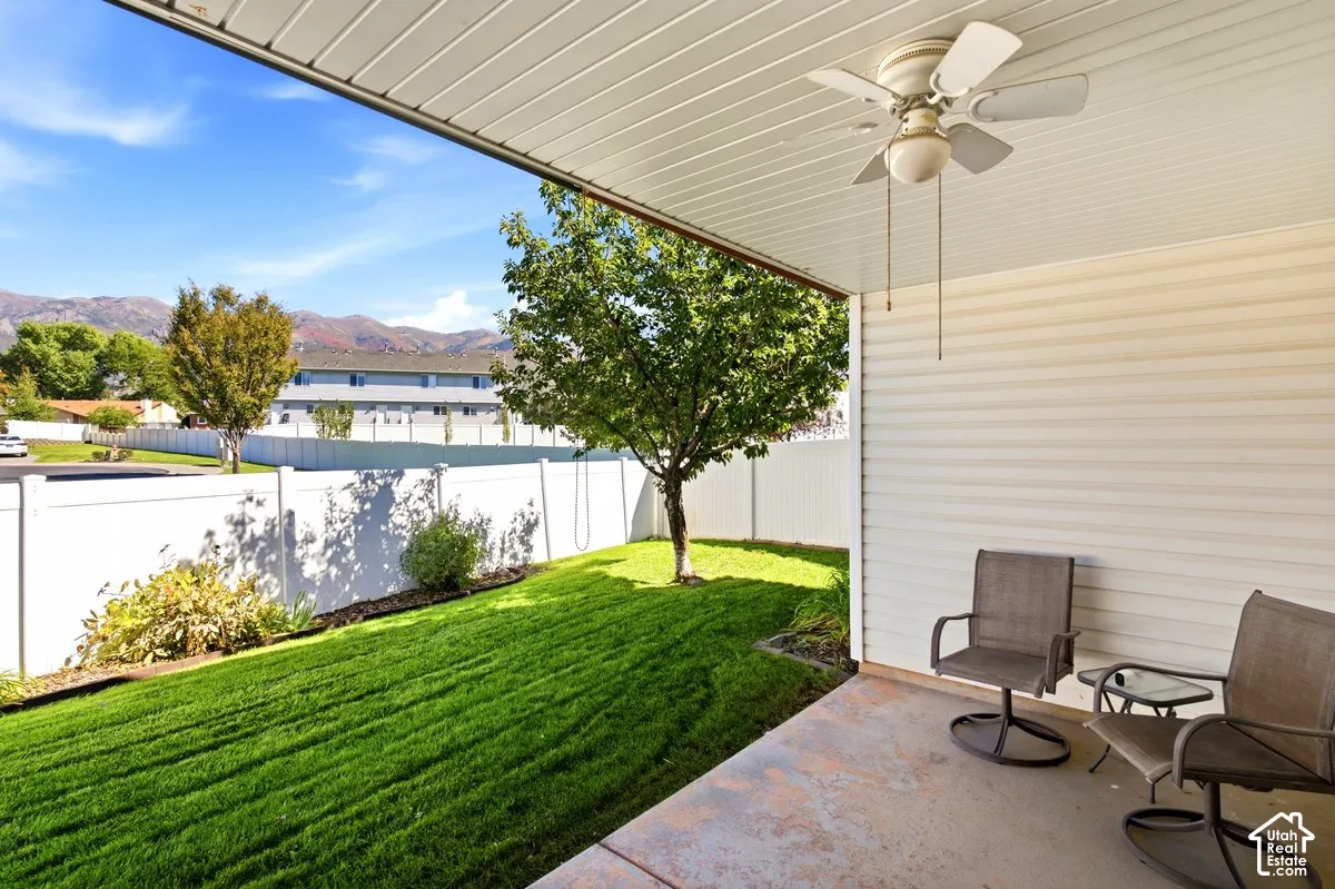 Covered patio with a built-in ceiling fan, concrete flooring, and a white vinyl privacy fence enclosing a manicured lawn