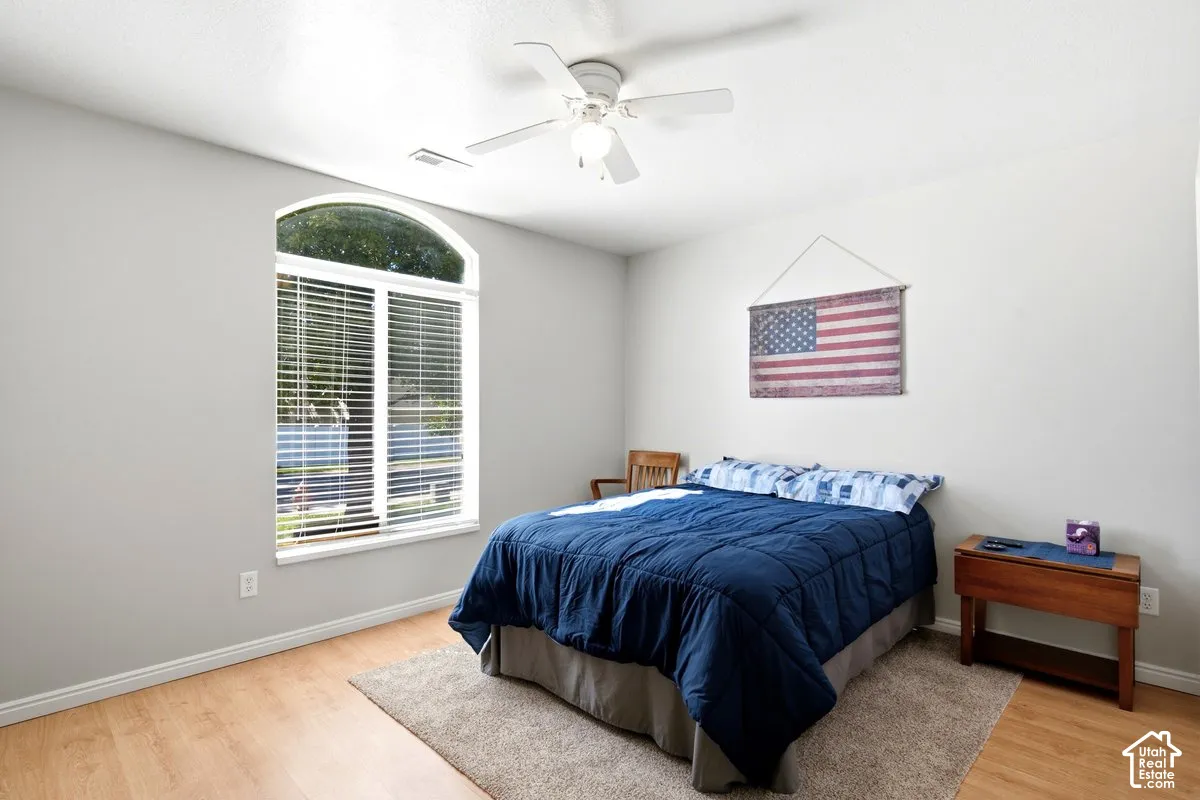 Arched window with blinds, wood-finish flooring, ceiling fan, and light gray wall finish