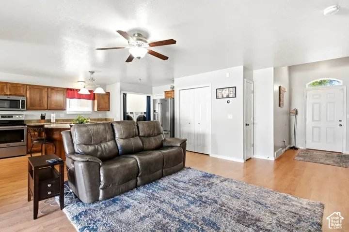 Open-concept living area featuring wood-finish flooring, a ceiling fan with integrated lighting, and a kitchen with stainless steel appliances